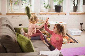 Image showing Young woman exercising fitness, aerobic, yoga at home, sporty lifestyle. Getting active with her child playing, home gym.