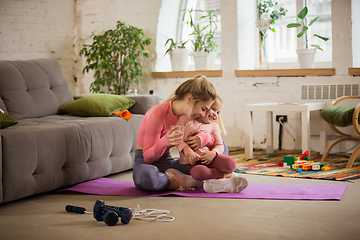 Image showing Young woman exercising fitness, aerobic, yoga at home, sporty lifestyle. Getting active while child, daughter playing with her, home gym.