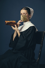 Image showing Medieval young woman as a nun in vintage clothing and golden face mask on dark blue background. Concept of comparison of eras, protection from covid