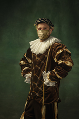 Image showing Portrait of medieval young man in vintage clothing and golden face mask standing on dark background.