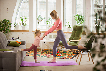 Image showing Young woman exercising fitness, aerobic, yoga at home, sporty lifestyle. Getting active with her child playing, home gym.