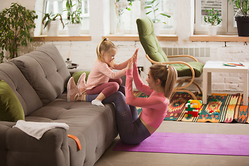 Image showing Young woman exercising fitness, aerobic, yoga at home, sporty lifestyle. Getting active with her child playing, home gym.