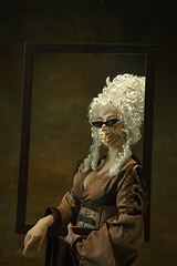 Image showing Portrait of medieval young woman in vintage clothes and golden face mask on dark background.