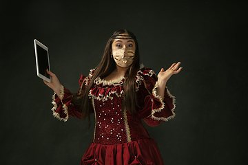 Image showing Portrait of medieval young woman in vintage clothes and golden face mask on dark background.