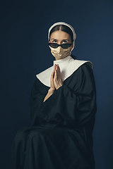 Image showing Medieval young woman as a nun in vintage clothing and golden face mask on dark blue background. Concept of comparison of eras, protection from covid