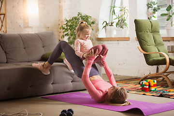 Image showing Young woman exercising fitness, aerobic, yoga at home, sporty lifestyle. Getting active with her child playing, home gym.