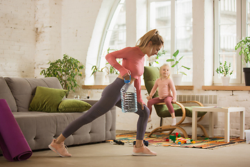 Image showing Young woman exercising fitness, aerobic, yoga at home, sporty lifestyle. Getting active with her child playing, home gym.