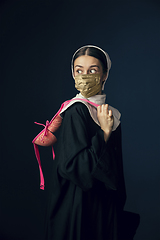 Image showing Medieval young woman as a nun in vintage clothing and golden face mask on dark blue background. Concept of comparison of eras, protection from covid