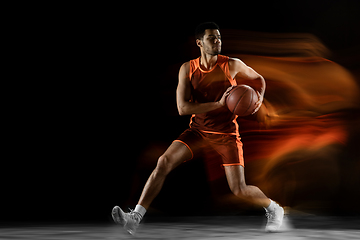 Image showing Young arabian basketball player of team in action, motion isolated on black background in mixed light. Concept of sport, movement, energy and dynamic.