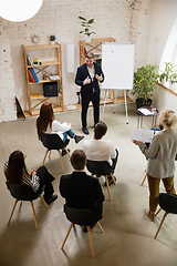 Image showing Male speaker giving presentation in hall at workshop. Audience or conference hall. High angle of unrecognized participants.