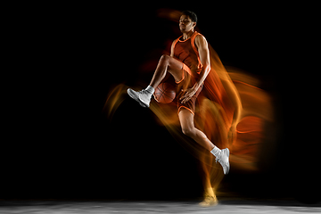 Image showing Young arabian basketball player of team in action, motion isolated on black background in mixed light. Concept of sport, movement, energy and dynamic.