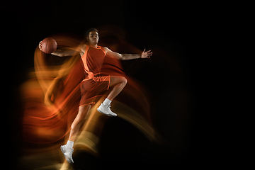 Image showing Young arabian basketball player of team in action, motion isolated on black background in mixed light. Concept of sport, movement, energy and dynamic.