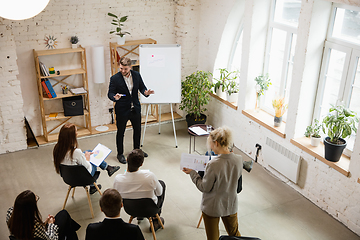 Image showing Male speaker giving presentation in hall at workshop. Audience or conference hall. High angle of unrecognized participants.