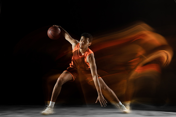 Image showing Young arabian basketball player of team in action, motion isolated on black background in mixed light. Concept of sport, movement, energy and dynamic.