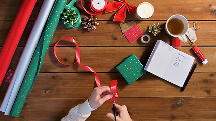 Image showing hands packing christmas gift and cutting ribbon