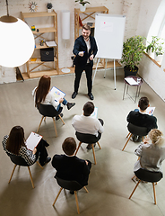 Image showing Male speaker giving presentation in hall at workshop. Audience or conference hall. High angle of unrecognized participants.