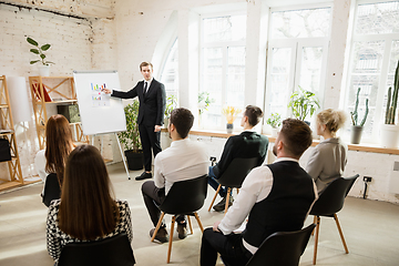 Image showing Male speaker giving presentation in hall at workshop. Audience or conference hall. Rear view of unrecognized participants.