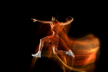 Image showing Young arabian basketball player of team in action, motion isolated on black background in mixed light. Concept of sport, movement, energy and dynamic.