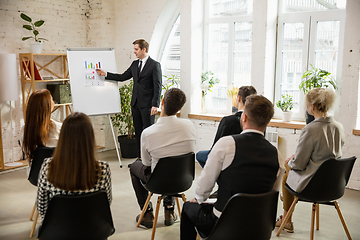 Image showing Male speaker giving presentation in hall at workshop. Audience or conference hall. Rear view of unrecognized participants.