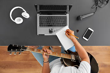 Image showing man with guitar writing to music book at table