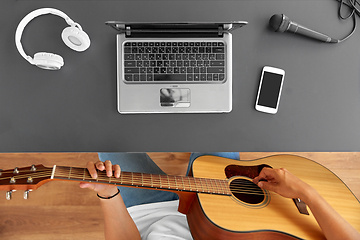 Image showing young man with laptop playing guitar at table