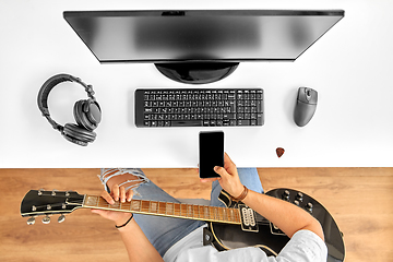 Image showing young man with guitar and smartphone at table