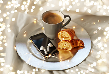 Image showing smartphone, earphones, coffee and croissant in bed