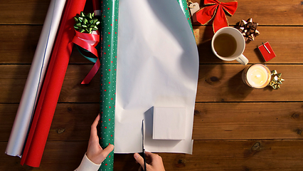 Image showing hands wrapping christmas gift into paper at home