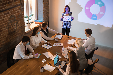 Image showing Female speaker giving presentation in hall at workshop. Audience or conference hall. Participants, co-workers listening at the table.