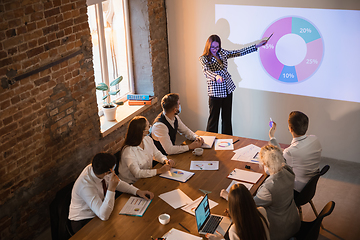 Image showing Female speaker giving presentation in hall at workshop. Audience or conference hall. Participants, co-workers listening at the table.