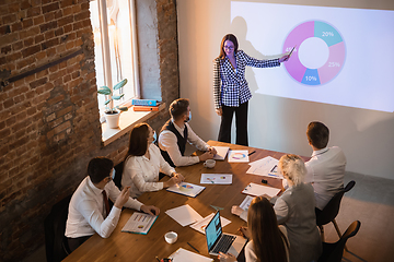 Image showing Female speaker giving presentation in hall at workshop. Audience or conference hall. Participants, co-workers listening at the table.