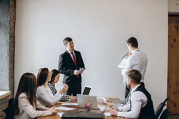 Image showing Male speaker giving presentation in hall at workshop. Audience or conference hall. Participants, co-workers listening at the table.