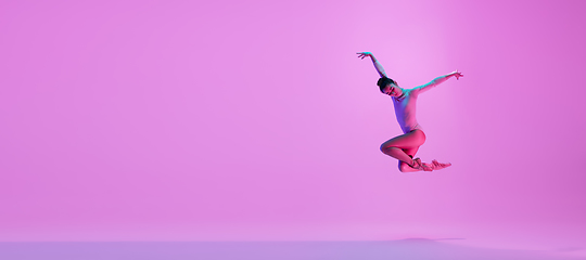 Image showing Young and graceful ballet dancer isolated on pink studio background in neon light. Art, motion, action, flexibility, inspiration concept.