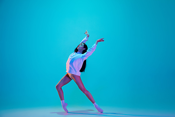 Image showing Young and graceful ballet dancer isolated on blue studio background in neon light. Art, motion, action, flexibility, inspiration concept.