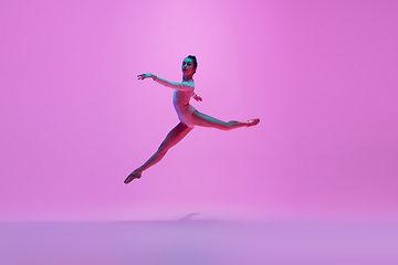 Image showing Young and graceful ballet dancer isolated on pink studio background in neon light. Art, motion, action, flexibility, inspiration concept.