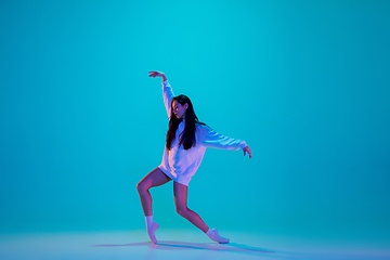 Image showing Young and graceful ballet dancer isolated on blue studio background in neon light. Art, motion, action, flexibility, inspiration concept.