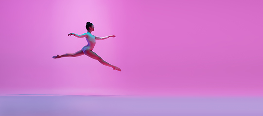 Image showing Young and graceful ballet dancer isolated on pink studio background in neon light. Art, motion, action, flexibility, inspiration concept.