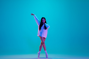 Image showing Young and graceful ballet dancer isolated on blue studio background in neon light. Art, motion, action, flexibility, inspiration concept.