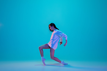 Image showing Young and graceful ballet dancer isolated on blue studio background in neon light. Art, motion, action, flexibility, inspiration concept.