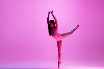 Image showing Young and graceful ballet dancer isolated on pink studio background in neon light. Art, motion, action, flexibility, inspiration concept.