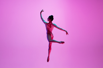 Image showing Young and graceful ballet dancer isolated on pink studio background in neon light. Art, motion, action, flexibility, inspiration concept.