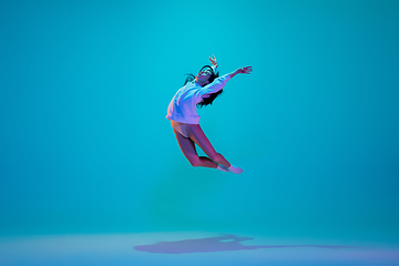 Image showing Young and graceful ballet dancer isolated on blue studio background in neon light. Art, motion, action, flexibility, inspiration concept.