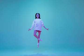 Image showing Young and graceful ballet dancer isolated on blue studio background in neon light. Art, motion, action, flexibility, inspiration concept.