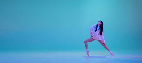 Image showing Young and graceful ballet dancer isolated on blue studio background in neon light. Art, motion, action, flexibility, inspiration concept.