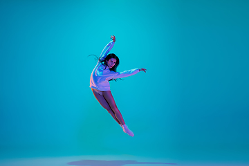 Image showing Young and graceful ballet dancer isolated on blue studio background in neon light. Art, motion, action, flexibility, inspiration concept.