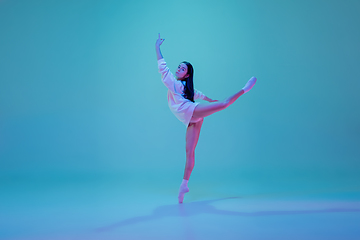 Image showing Young and graceful ballet dancer isolated on blue studio background in neon light. Art, motion, action, flexibility, inspiration concept.