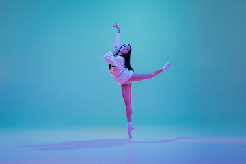 Image showing Young and graceful ballet dancer isolated on blue studio background in neon light. Art, motion, action, flexibility, inspiration concept.