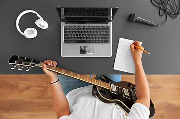 Image showing man with guitar writing to music book at table