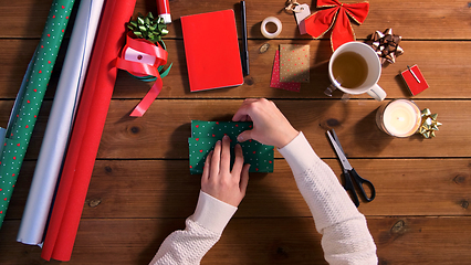 Image showing hands wrapping christmas gift into paper at home