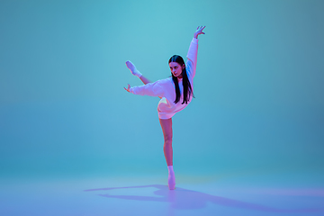 Image showing Young and graceful ballet dancer isolated on blue studio background in neon light. Art, motion, action, flexibility, inspiration concept.